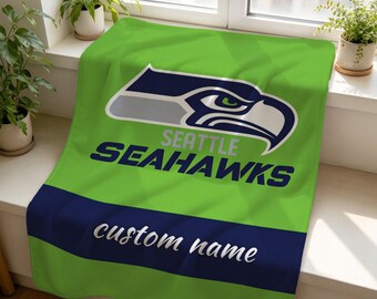 Könnte beinhalten: Eine leuchtend hellgrüne Fleecedecke mit dem Seattle Seahawks-Logo in Marineblau, Grau und Weiß. Unter dem Logo steht der Text SEATTLE SEAHAWKS. Ein horizontaler marineblauer Streifen am unteren Rand enthält den Text custom name.