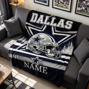 May include: A navy blue and silver fleece throw blanket featuring a large Dallas Cowboys football helmet graphic, a prominent star logo, the word DALLAS in bold white lettering at the top, and the word NAME in white text at the bottom.