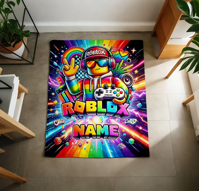 May include: A rectangular blanket featuring a vibrant rainbow-colored graphic of a character wearing headphones, sunglasses, and a cap, holding a game controller. The design includes the text ROBLOX and NAME, surrounded by colorful light streaks.