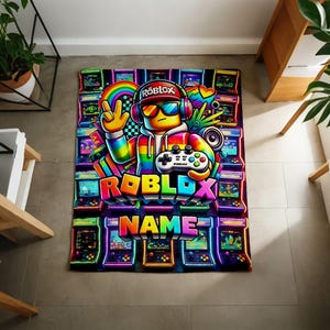 May include: A rectangular blanket featuring a vibrant, neon-colored graphic of a Roblox character wearing headphones and sunglasses, holding a game controller. The design includes multiple arcade cabinets, a rainbow, and the text Roblox and Name.