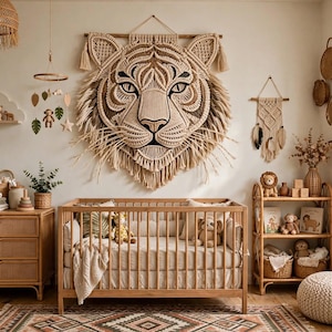 May include: A large macrame tiger head wall hanging with intricate knotting and fringe, displayed above a wooden crib. The room features a rattan dresser, a shelving unit with plush toys, a woven mobile, and a smaller macrame wall piece.