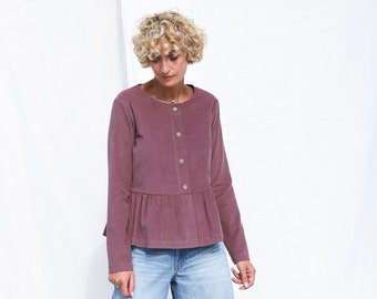 May include: A mauve long-sleeved top with a round neckline, a button-down front, and a gathered peplum waist, paired with light blue wide-leg denim jeans. The top features a textured fabric and light-colored buttons down the center front.