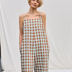 May include: A woman wearing a brown and light blue gingham jumpsuit. The jumpsuit has thin straps and a square neckline.