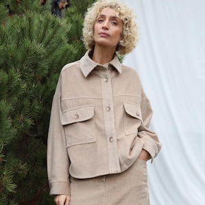 May include: A beige corduroy jacket and skirt co-ord. The jacket features two chest pockets and button fastenings. The midi-length skirt has a front split. The outfit is a neutral colour and appears to be made of a soft, textured fabric.