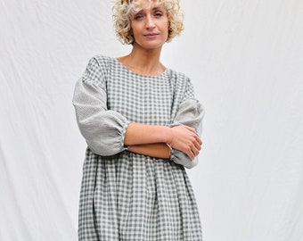 May include: A woman wearing a green and white gingham dress with puffed sleeves. The dress has a loose fit and falls to her knees.