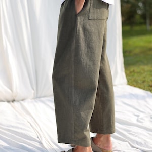 May include: A pair of olive green linen pants with a wide leg and a relaxed fit. The pants have a simple design with a single pocket on the right side.