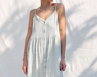 Könnte beinhalten: Ein hellblaues und weißes Gingham-Midikleid mit Knopfleiste vorne und dünnen Trägern.