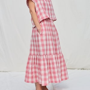 May include: A pink and white gingham top and skirt set. The top has short sleeves and a relaxed fit. The skirt is a midi length with a ruffled hem.
