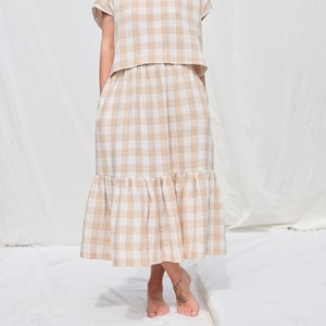 May include: A beige and white gingham dress with a ruffled hem. The dress has a fitted bodice and a flowy skirt.
