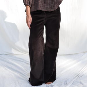 May include: A brown plaid blouse with long sleeves and a button-down front is paired with wide-leg corduroy pants. The outfit is a neutral color palette, with a relaxed fit. The blouse has a round neckline.