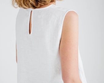 Puede incluir: Una blusa sin mangas de lino blanco con cuello redondo y una pequeña abertura en forma de cerradura en la parte superior de la espalda con un cierre de un solo botón. La prenda tiene un dobladillo recto y se combina con pantalones negros.
