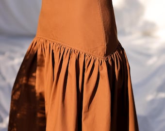 May include: A brown, full-length skirt with a gathered, ruffled hem. The skirt has a fitted waistband and a back zipper closure.