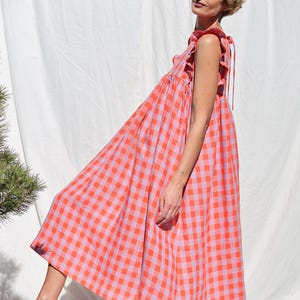 Op de afbeelding: Een roze en oranje gingham midi-jurk met een gerimpelde halslijn en bandjes. De jurk heeft een losse, zwierige pasvorm.