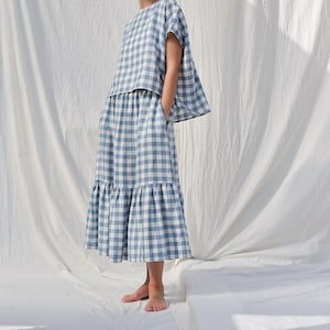 May include: A two-piece outfit in a blue and white gingham pattern. The top is a loose-fitting, short-sleeved blouse. The skirt is a midi-length with a ruffled hem. The outfit is made of a lightweight fabric, perfect for warm weather.
