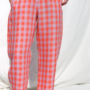 May include: A pair of wide-leg pants with a gingham pattern in shades of pink and orange. The pants have an elastic waistband and a relaxed fit.