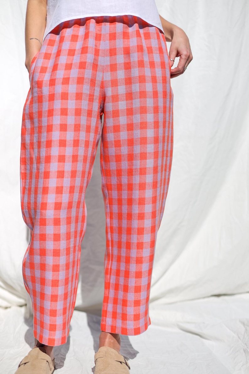 May include: A pair of wide-leg pants with a gingham pattern in shades of pink and orange. The pants have an elastic waistband and a relaxed fit.