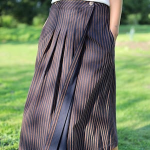 May include: A navy and brown striped skirt with a wrap-style design. The skirt features vertical stripes and a button closure. The garment is made of a lightweight fabric and has a pleated detail.