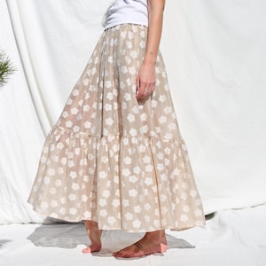 May include: A beige maxi skirt with a white floral pattern. The skirt has a tiered design and a flowy silhouette.