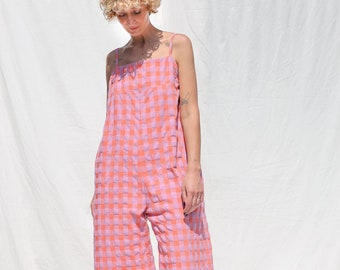 May include: A pink and orange gingham jumpsuit with thin straps. The jumpsuit has a relaxed fit and wide legs.