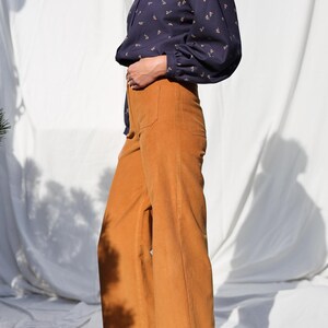 May include: A woman wearing a navy blue blouse with a white collar and a floral print. She is also wearing wide-leg, mustard yellow corduroy pants.