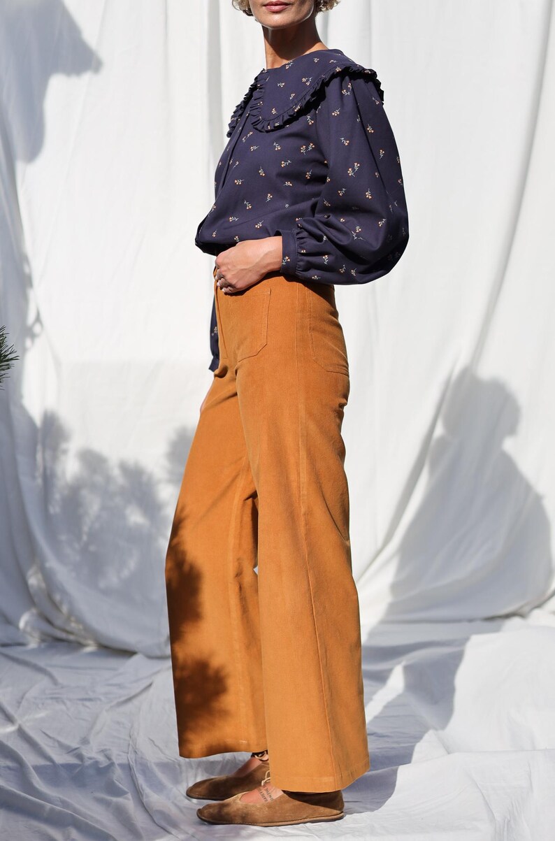 May include: A woman wearing a navy blue blouse with a white collar and a floral print. She is also wearing wide-leg, mustard yellow corduroy pants.