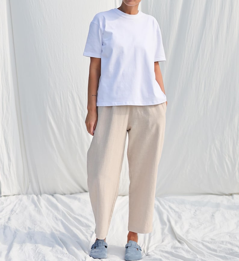Puede incluir: Una camiseta blanca de gran tama&ntilde;o con mangas cortas y un corte holgado combinada con pantalones beige de pierna ancha. La modelo lleva zapatos planos de color azul claro.