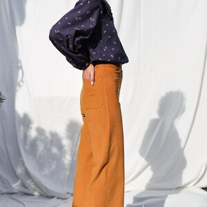May include: A woman wearing a navy blue blouse with a floral print and a white collar, paired with wide-leg, mustard yellow corduroy pants.