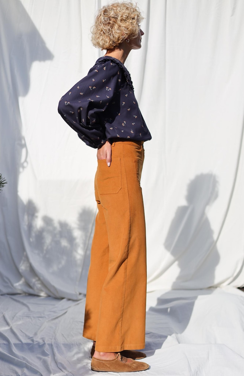 May include: A woman wearing a navy blue blouse with a floral print and a white collar, paired with wide-leg, mustard yellow corduroy pants.