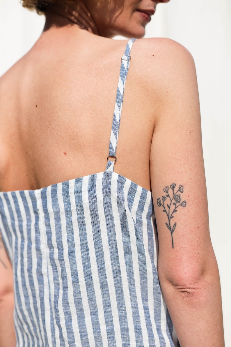 Puede incluir: Una mujer con un vestido de lino a rayas azules y blancas con una tira fina. Tiene un peque&ntilde;o tatuaje de flor en la parte superior del brazo.