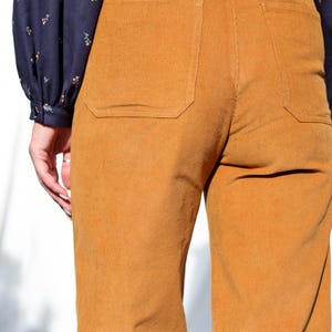 May include: A pair of brown corduroy pants with a patch pocket on the back. The pants have a wide leg and a relaxed fit.