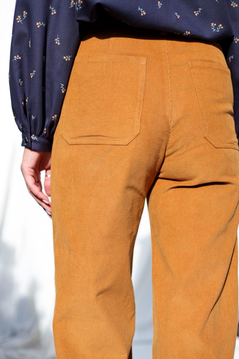 May include: A pair of brown corduroy pants with a patch pocket on the back. The pants have a wide leg and a relaxed fit.