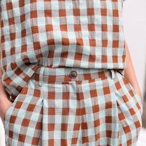 May include: A pair of brown and light blue checkered pants with a button closure. The pants have pleats in the front and are made of a lightweight fabric.