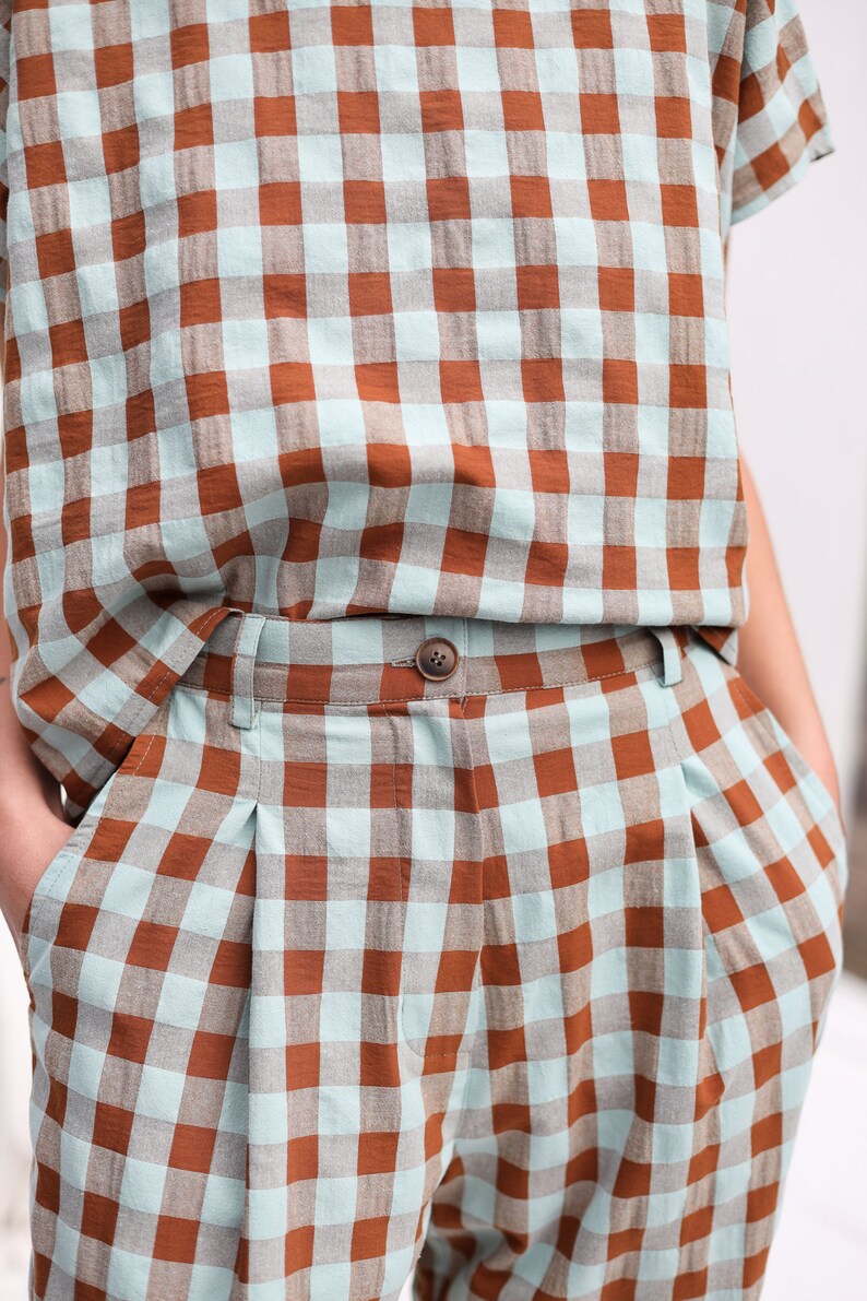 May include: A pair of brown and light blue checkered pants with a button closure. The pants have pleats in the front and are made of a lightweight fabric.