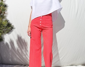 May include: A white linen top with short sleeves and a loose fit, paired with wide-leg pants in a pink and white gingham pattern.