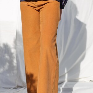 May include: A pair of wide-leg corduroy pants in a mustard yellow color. The pants have a straight leg and a relaxed fit. The model is wearing the pants with a navy blue floral print shirt and brown leather shoes.