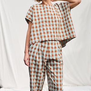 May include: A woman wearing a brown and blue gingham top and matching pants. The top has a relaxed fit and short sleeves. The pants are cropped and have a pleated waistband.
