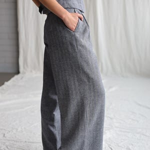 Puede incluir: Pantalón ancho gris con un sutil patrón de espiga. El pantalón tiene un pliegue delantero y un bolsillo lateral.