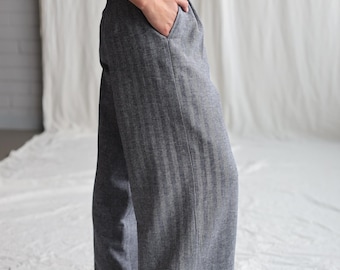 May include: Gray wide-leg pants with a subtle herringbone pattern. The pants have a front pleat and a side pocket.