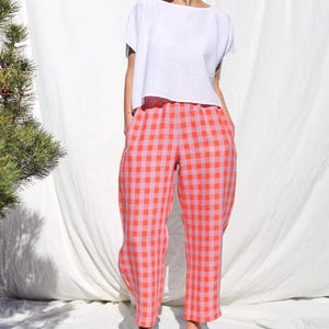 May include: A white linen top with short sleeves and a relaxed fit, paired with pink and orange gingham pants.
