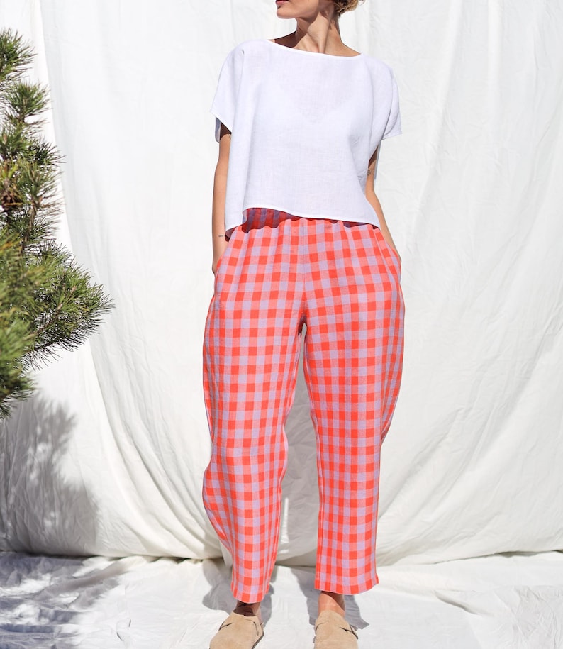 May include: A white linen top with short sleeves and a relaxed fit, paired with pink and orange gingham pants.