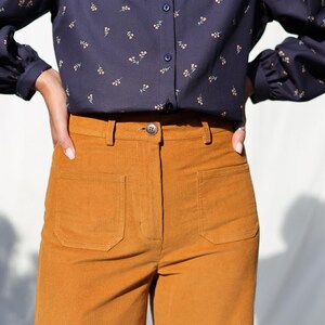 May include: A pair of high-waisted, wide-leg corduroy pants in a rich mustard yellow color. The pants have a button fly and two large patch pockets on the front.
