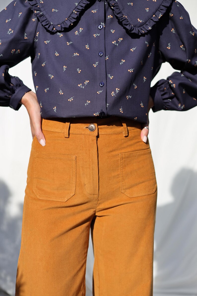 May include: A pair of high-waisted, wide-leg corduroy pants in a rich mustard yellow color. The pants have a button fly and two large patch pockets on the front.