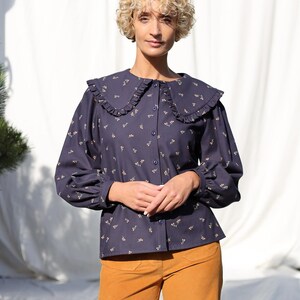 May include: A navy blue blouse with a white ruffled collar and a floral print. The blouse has long sleeves and a button-up front.