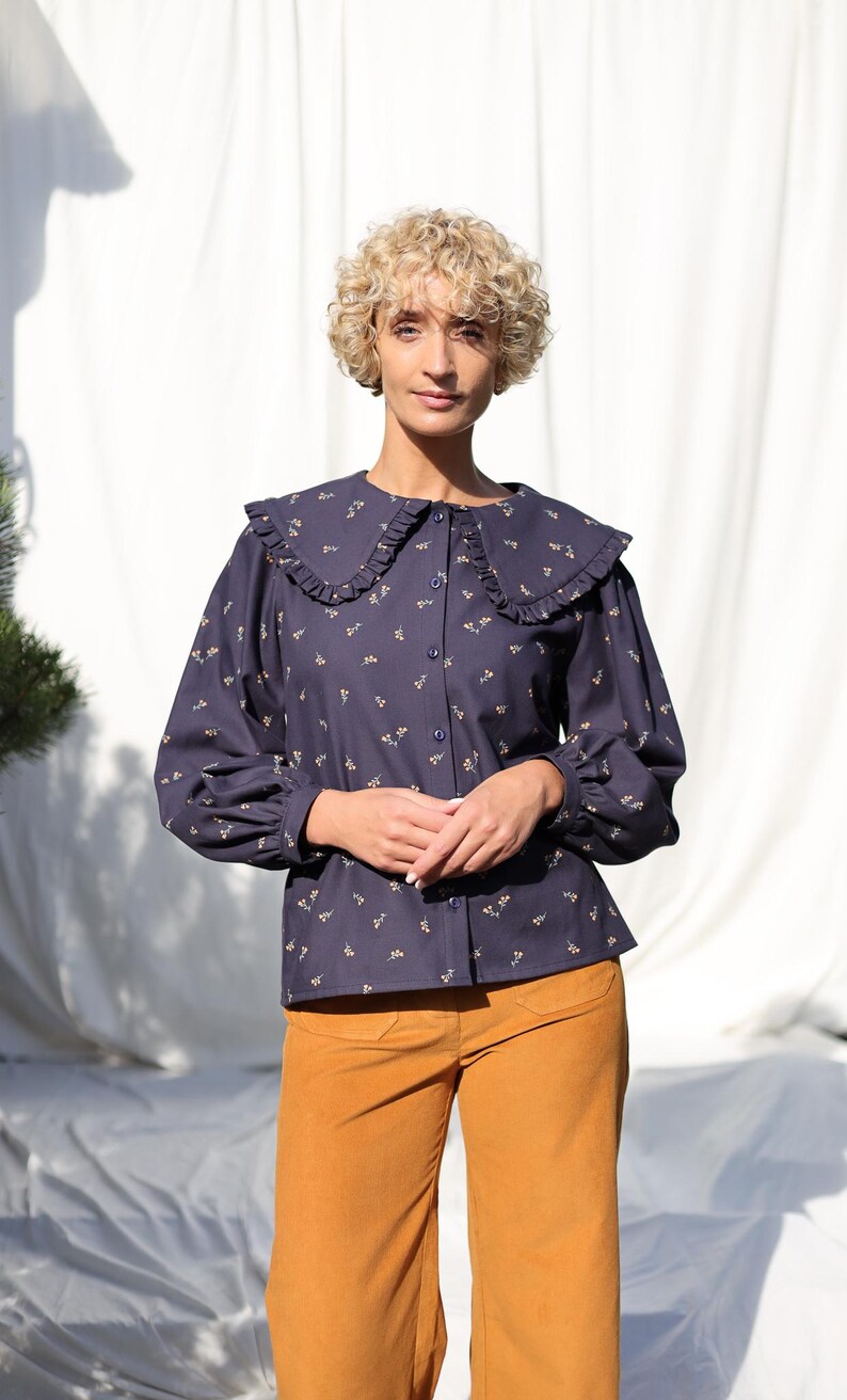 May include: A navy blue blouse with a white ruffled collar and a floral print. The blouse has long sleeves and a button-up front.