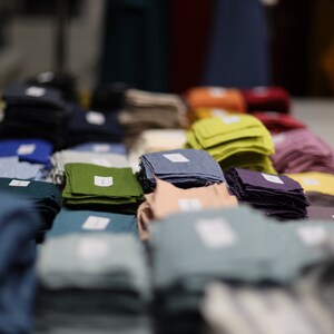 Może przedstawiać: R&oacute;żne pr&oacute;bki tkanin w r&oacute;żnych kolorach i fakturach, ułożone w stosy i oznaczone etykietami. Pr&oacute;bki obejmują odcienie niebieskiego, zielonego, fioletowego, r&oacute;żowego i ż&oacute;łtego.