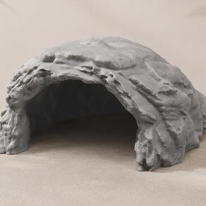 May include: A grey, rock-shaped reptile hide with a textured, uneven surface and a large, arched opening. The structure features realistic, jagged edges and a hollow interior, designed to mimic a natural stone cave for small animals.