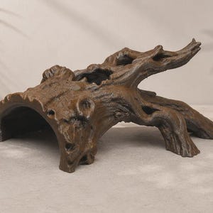 May include: A brown, hollowed-out log ornament featuring a textured, bark-like surface with a large arched opening on one side and a protruding, branch-like extension on the other, designed as a shelter for small animals or aquatic pets.
