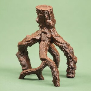 Puede incluir: Una figura de tocón de árbol marrón de tres patas con una superficie texturizada similar a la corteza. El objeto presenta una sección de tronco vertical central que se ramifica en tres patas distintas en forma de raíces nudosas.