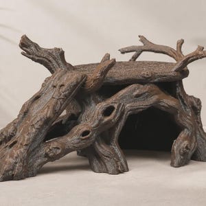 May include: A brown, textured reptile hide shaped like a hollowed-out tree stump with a flat top platform and a wide arched entrance. The surface features realistic bark detailing with deep grooves and knots, creating a natural appearance.