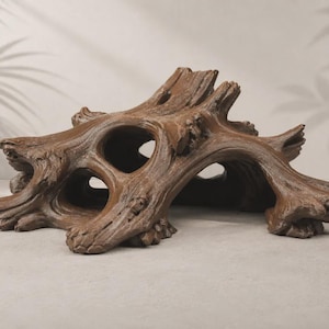 May include: A brown, hollowed-out tree stump ornament with a textured, bark-like surface. The piece features multiple openings and arched sections, mimicking the appearance of weathered driftwood with intricate knots and gnarled wood grain details.